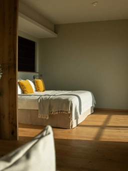 Blick auf ein bequemes Doppelbett, was sich in einem Zimmer vor einer großen Fensterfront steht und zum Übernachten im Rheingau einlädt