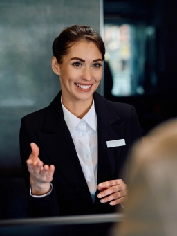 A smiling young woman in a business outfit greets a guest as part of her hotel job near Frankfurt